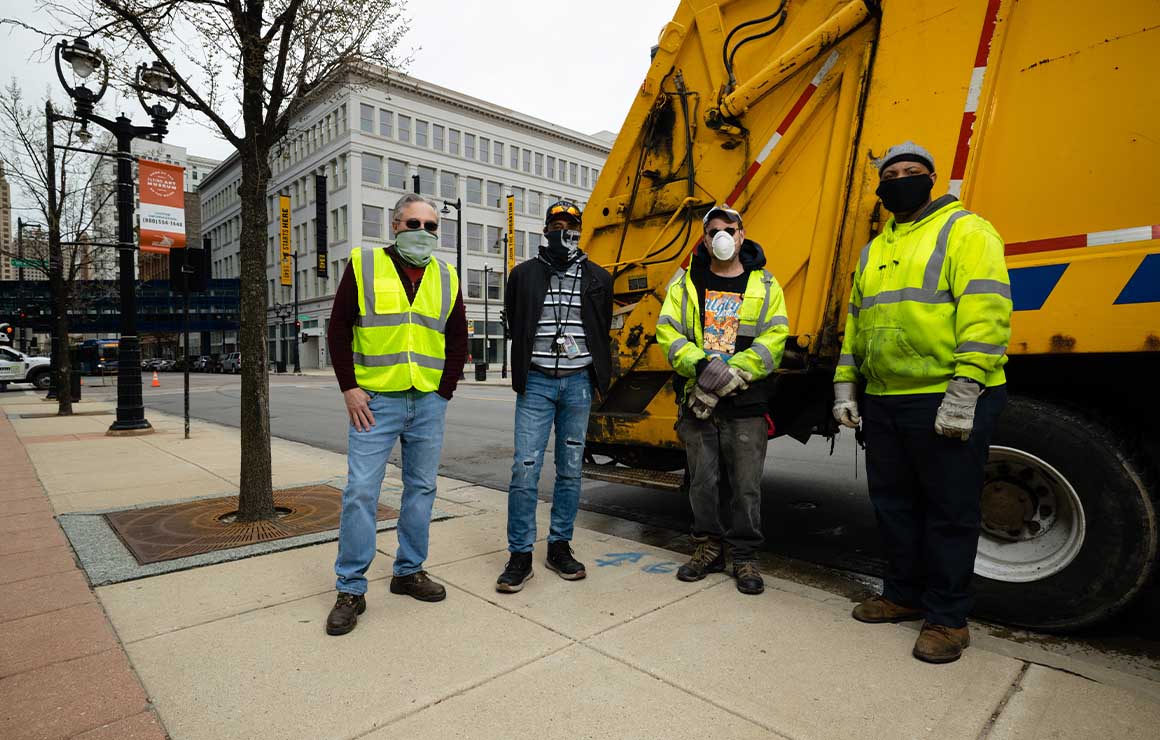 Members of the Department of Public Works stand in front of a garbage truck.