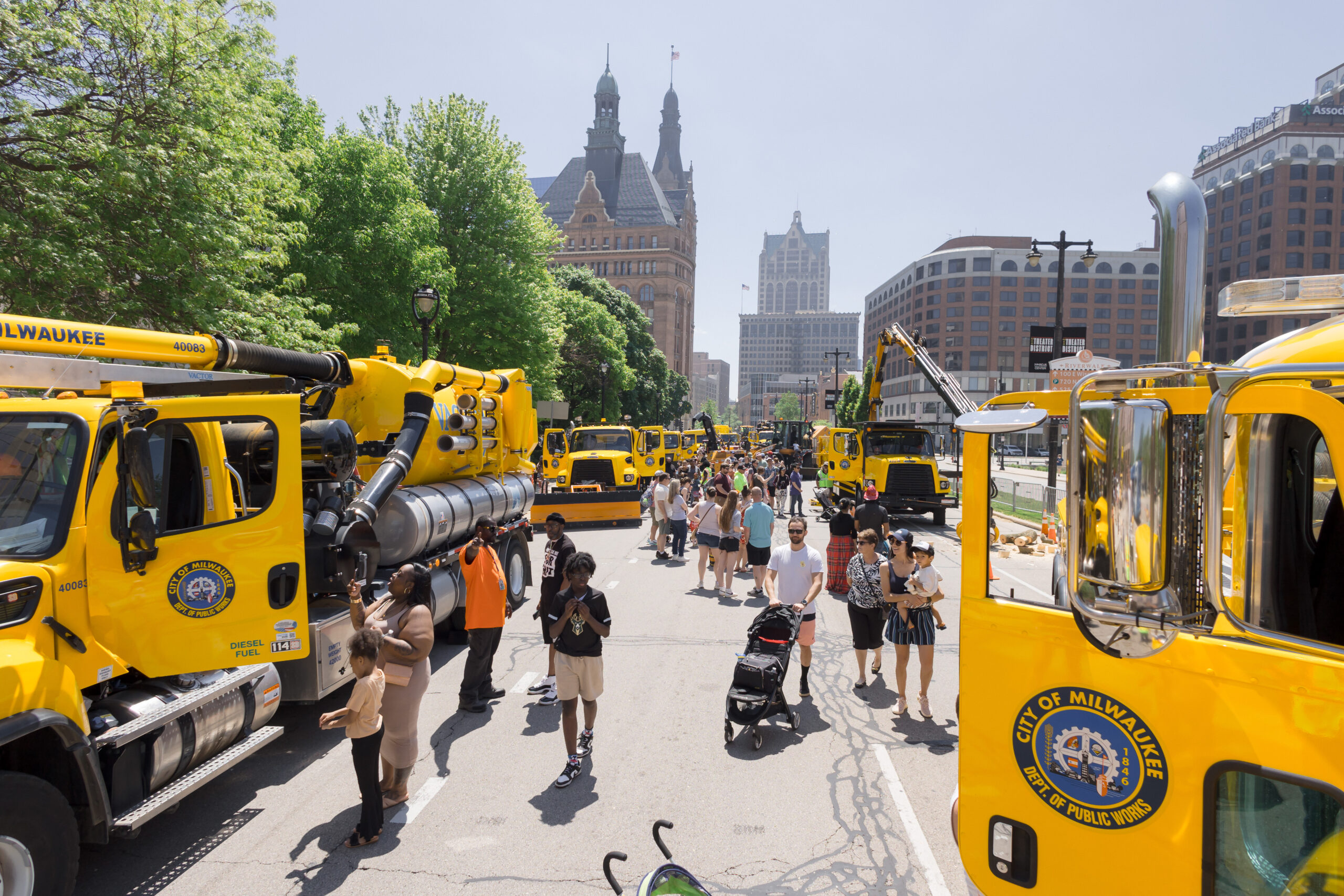 A crowd of people wander around among yellow city trucks for Big Truck Day.