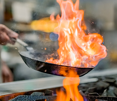 A chef holds a frying pan that's in flames.