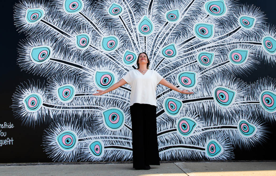 The artist stands in front of the What Lifts You mural.